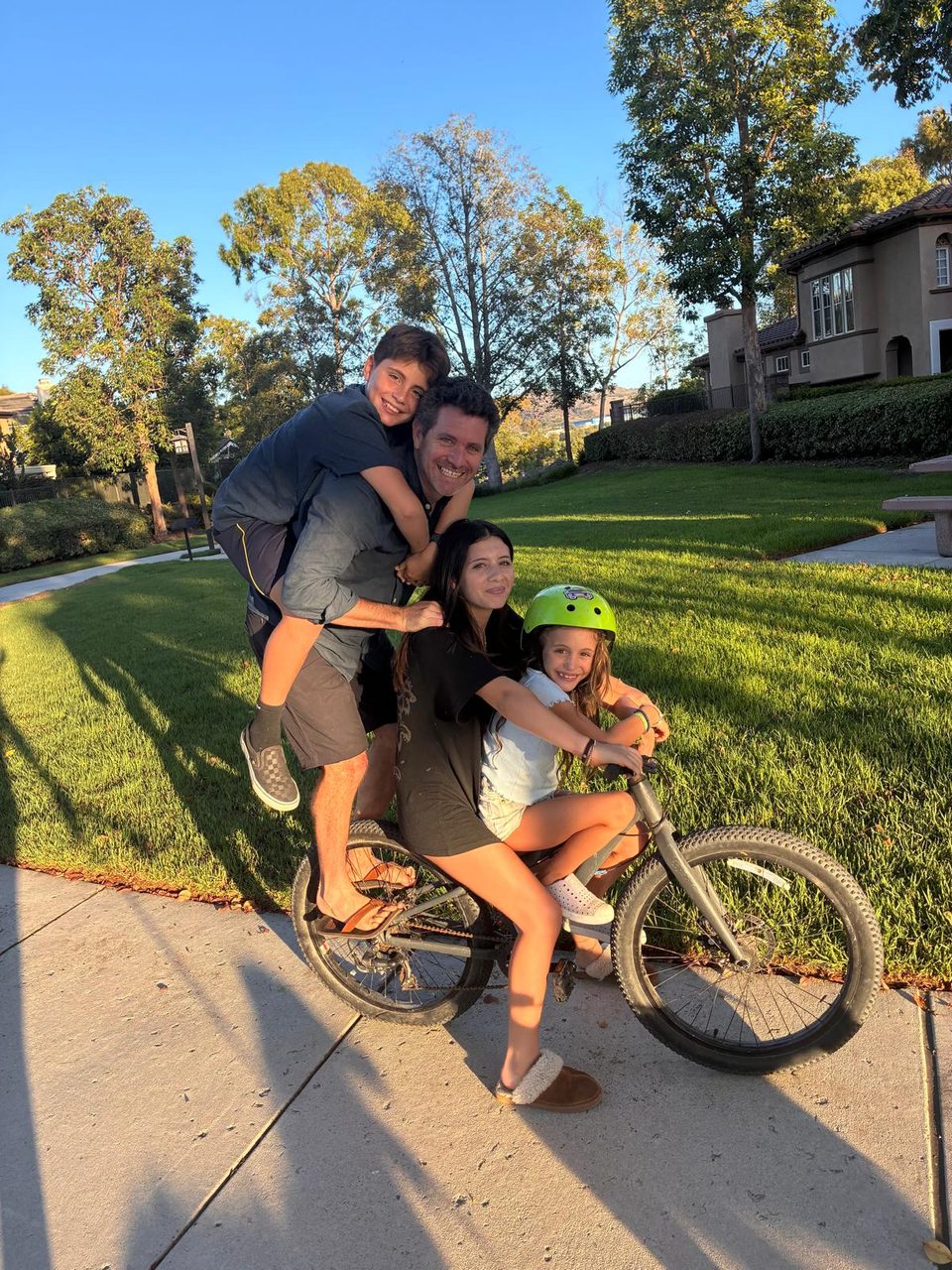 Josh and his three kids piled onto one bike on a sunny sidewalk